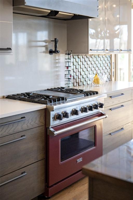 kitchen with under cabinet range hood, high end stove, gray cabinetry, and light countertops