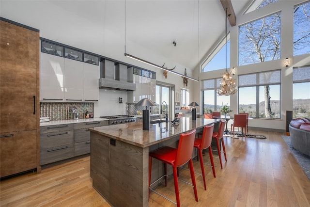 kitchen featuring a breakfast bar area, light wood finished floors, stainless steel gas cooktop, wall chimney range hood, and tasteful backsplash