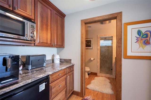 kitchen featuring light wood finished floors, stone counters, dishwasher, stainless steel microwave, and brown cabinets