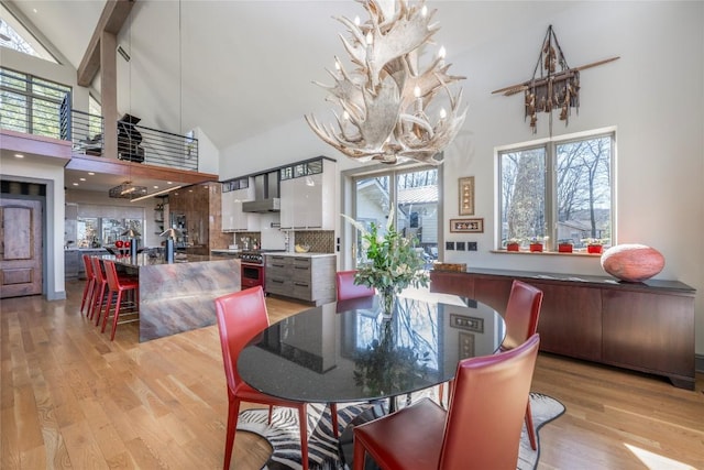 dining space with light wood finished floors, a notable chandelier, high vaulted ceiling, and a wealth of natural light