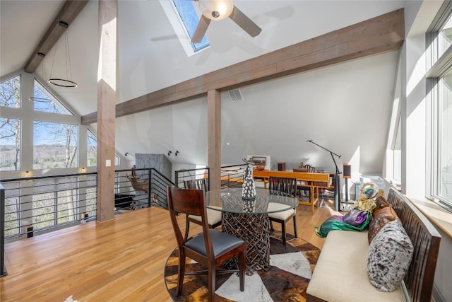 dining room featuring beamed ceiling, high vaulted ceiling, a ceiling fan, wood finished floors, and a skylight