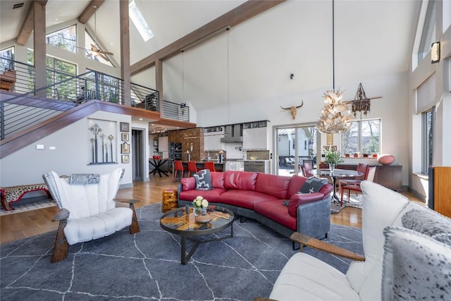 living room featuring stairs, beamed ceiling, a notable chandelier, and wood finished floors