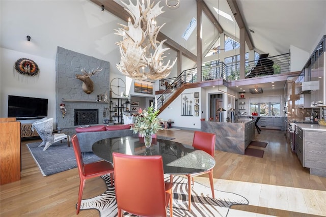 dining room featuring beam ceiling, high vaulted ceiling, a fireplace, light wood finished floors, and stairs