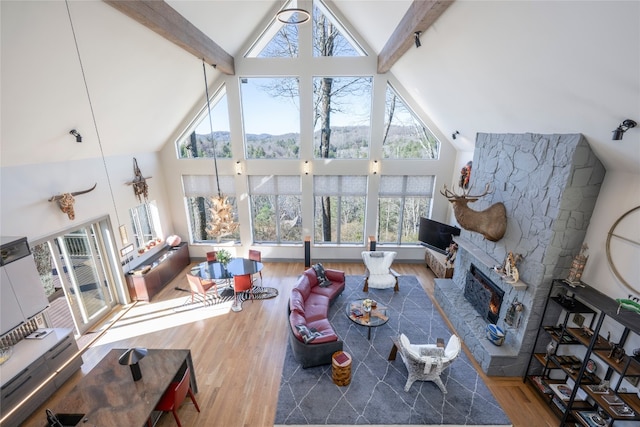 living room with a stone fireplace, beam ceiling, wood finished floors, and high vaulted ceiling