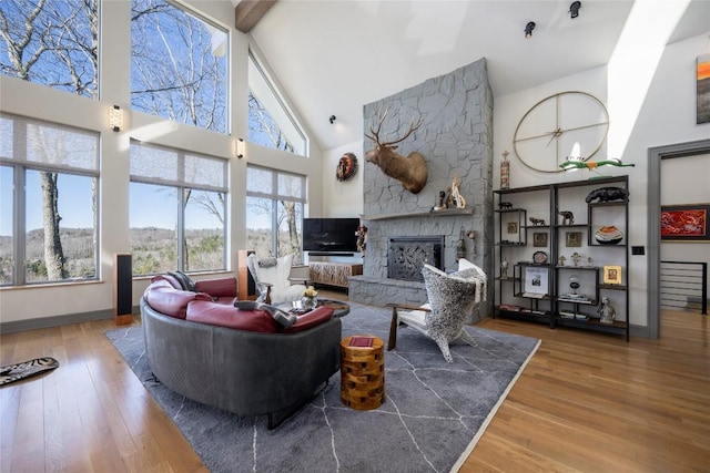 living area with baseboards, high vaulted ceiling, a stone fireplace, and wood finished floors