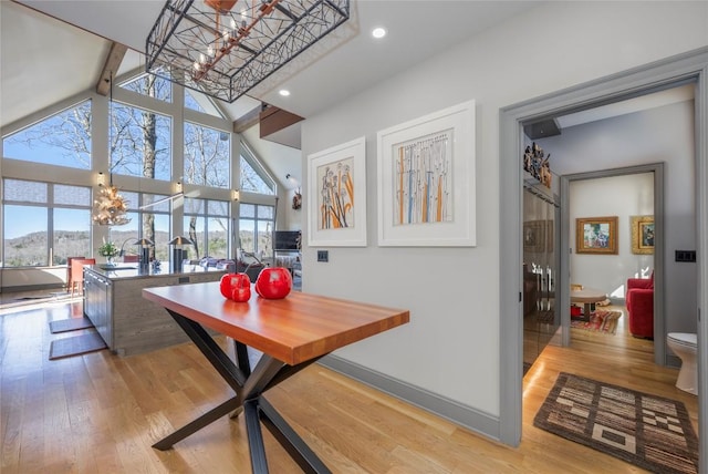 dining space featuring baseboards, recessed lighting, wood finished floors, a notable chandelier, and high vaulted ceiling