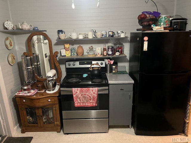 kitchen with black refrigerator, wooden walls, and stainless steel range with electric cooktop