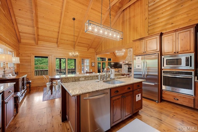 kitchen featuring sink, built in appliances, a center island with sink, decorative light fixtures, and wood walls