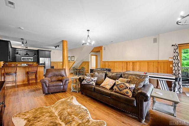 living room with an inviting chandelier, light hardwood / wood-style flooring, and wooden walls