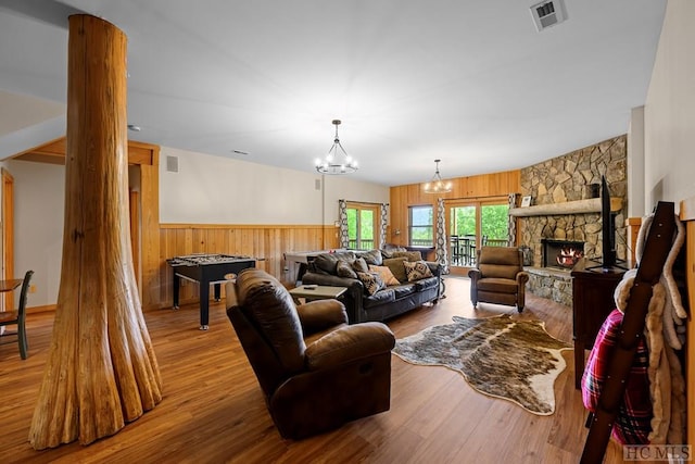 living room featuring wood-type flooring, wooden walls, a stone fireplace, and a notable chandelier