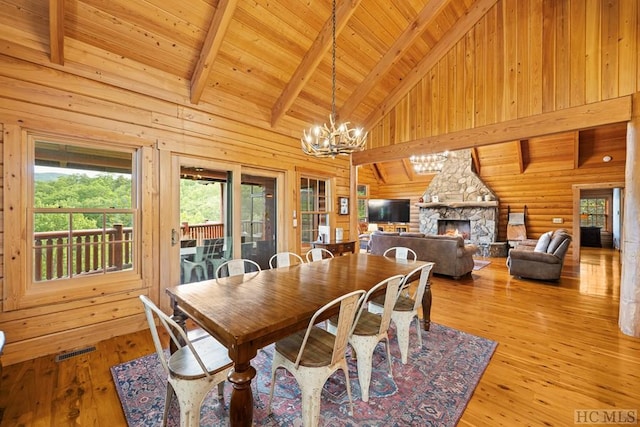 dining area featuring wood ceiling, a stone fireplace, light hardwood / wood-style flooring, and beamed ceiling