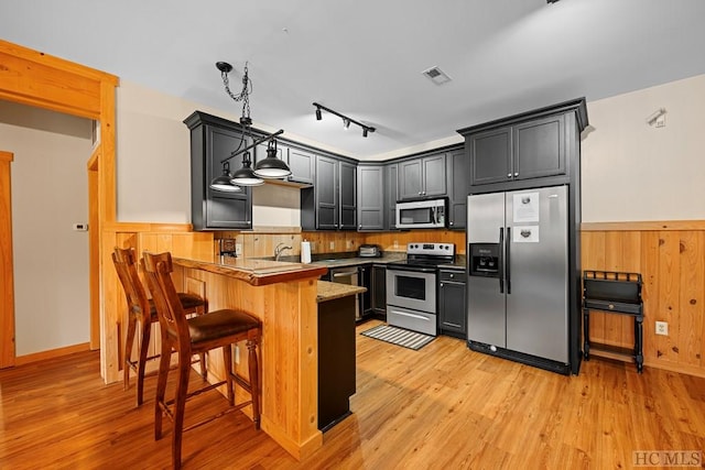 kitchen featuring pendant lighting, appliances with stainless steel finishes, a kitchen bar, kitchen peninsula, and light wood-type flooring