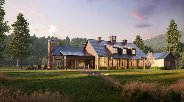 rear view of property with a standing seam roof, a chimney, a yard, and metal roof