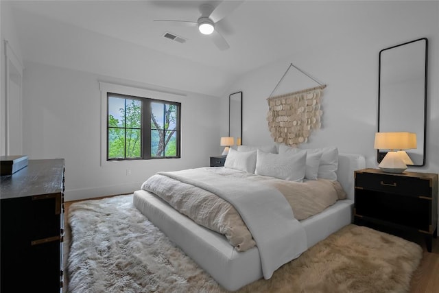 bedroom with ceiling fan, visible vents, vaulted ceiling, wood finished floors, and baseboards