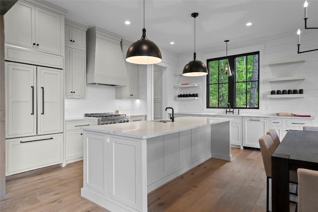 kitchen with open shelves, custom exhaust hood, light wood-type flooring, light countertops, and a sink