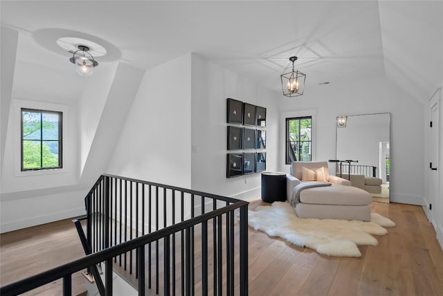 living area with vaulted ceiling, plenty of natural light, wood finished floors, and an upstairs landing