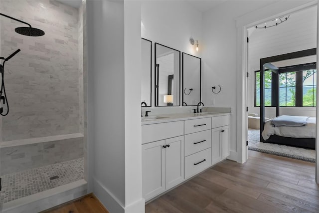 bathroom with a sink, double vanity, a tile shower, and wood finished floors