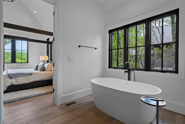 bathroom featuring visible vents, a freestanding tub, plenty of natural light, and wood finished floors