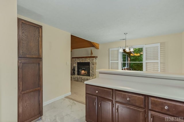 kitchen with dark brown cabinetry, an inviting chandelier, decorative light fixtures, beamed ceiling, and a fireplace