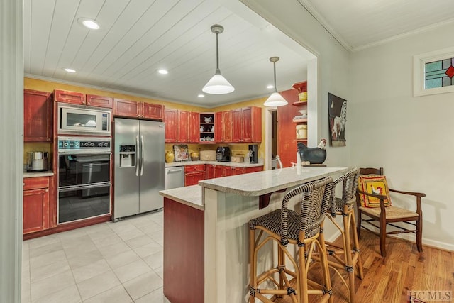 kitchen with appliances with stainless steel finishes, a breakfast bar, crown molding, kitchen peninsula, and hanging light fixtures