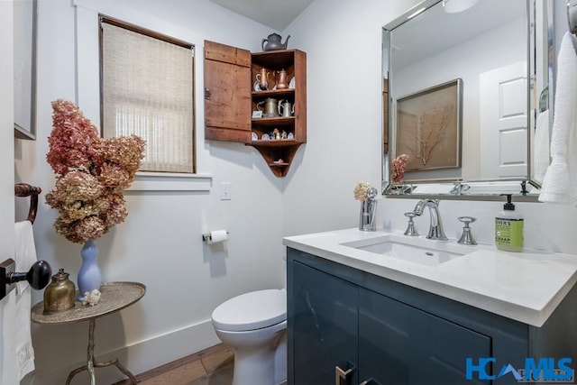 bathroom with baseboards, toilet, wood finished floors, and vanity