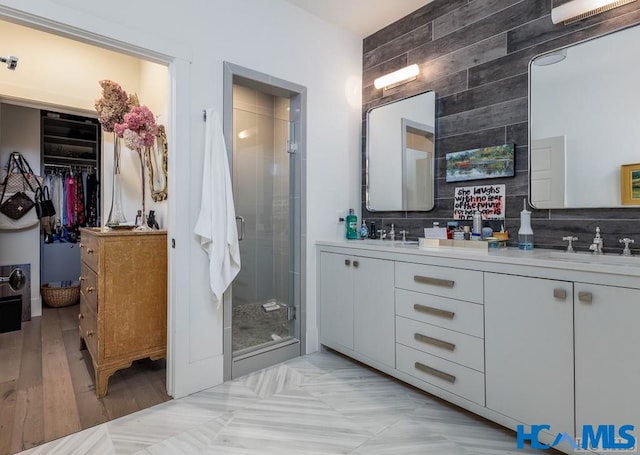 full bathroom featuring a walk in closet, double vanity, a stall shower, and a sink