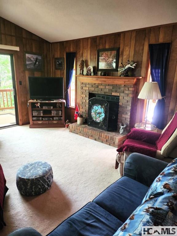 carpeted living room with wood walls, a brick fireplace, and lofted ceiling