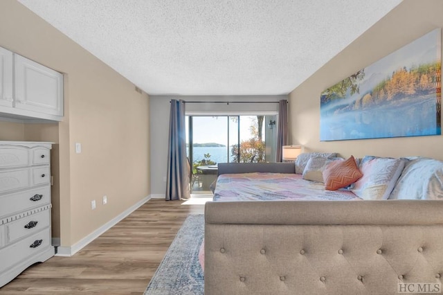 bedroom featuring access to outside, light hardwood / wood-style flooring, a textured ceiling, and a water view