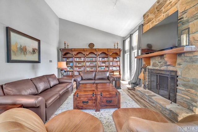 living room featuring rail lighting, a stone fireplace, and high vaulted ceiling