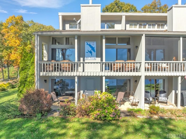 rear view of house with a lawn, a patio, and a balcony