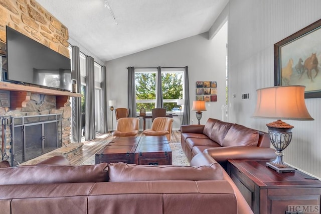 living room featuring hardwood / wood-style flooring, a stone fireplace, and vaulted ceiling