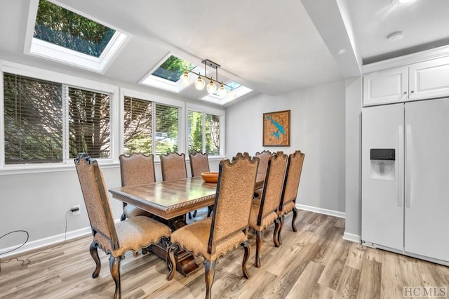 dining space with lofted ceiling with skylight and light wood-type flooring