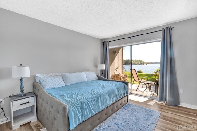 bedroom with access to exterior, light hardwood / wood-style floors, a textured ceiling, and a water view