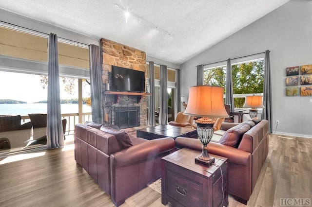 living room featuring vaulted ceiling, a stone fireplace, plenty of natural light, hardwood / wood-style flooring, and a water view