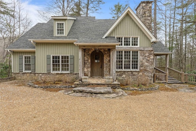 view of front of home featuring stone siding, board and batten siding, a chimney, and a shingled roof