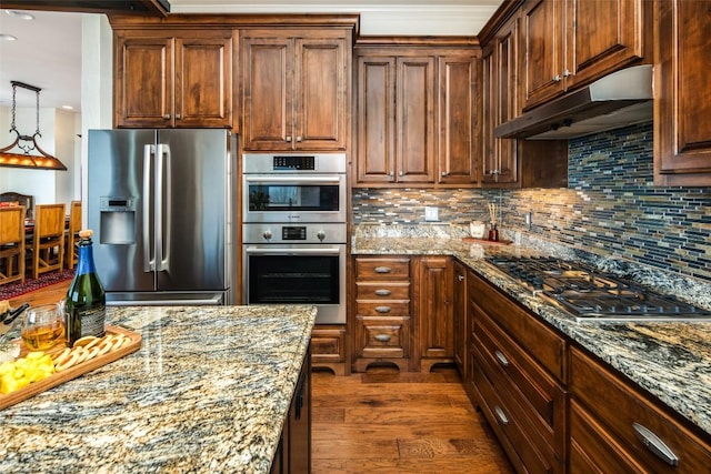 kitchen with appliances with stainless steel finishes, under cabinet range hood, backsplash, light stone countertops, and dark wood-type flooring