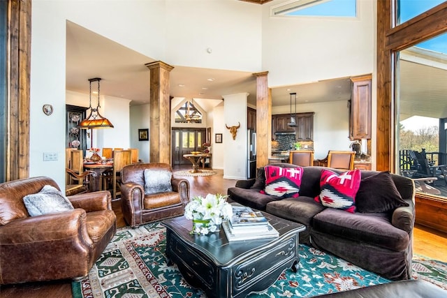 living room featuring wood finished floors, ornate columns, plenty of natural light, and a high ceiling