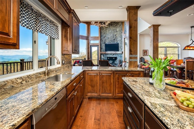 kitchen featuring dishwasher, a sink, dark wood-type flooring, a large fireplace, and ornate columns