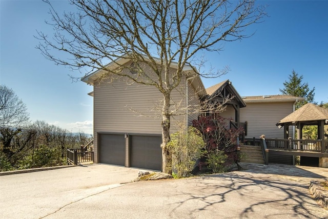 view of property exterior with an attached garage, a gazebo, and concrete driveway