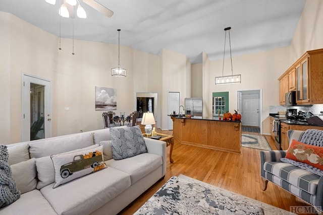 living room featuring ceiling fan, sink, light hardwood / wood-style floors, and a towering ceiling