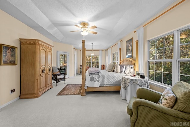 carpeted bedroom with a raised ceiling, ceiling fan, multiple windows, and a textured ceiling