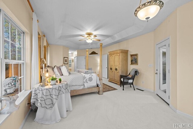 carpeted bedroom with ceiling fan, access to exterior, and a raised ceiling