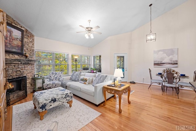 living room with ceiling fan, lofted ceiling, a stone fireplace, and light wood-type flooring