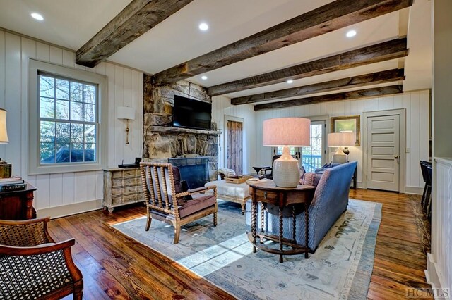 living room with dark hardwood / wood-style flooring, beam ceiling, and a stone fireplace