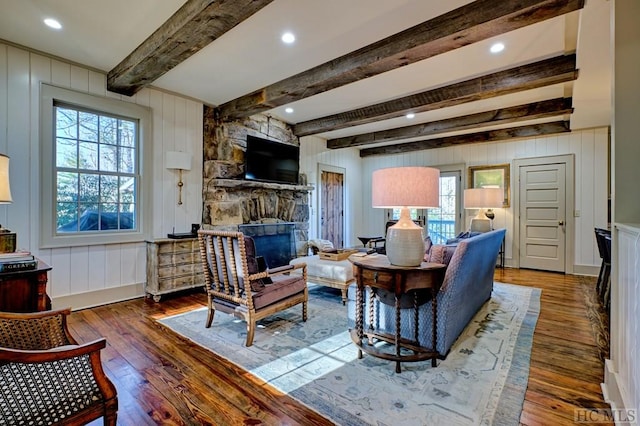 living room with beamed ceiling, a stone fireplace, and dark hardwood / wood-style floors