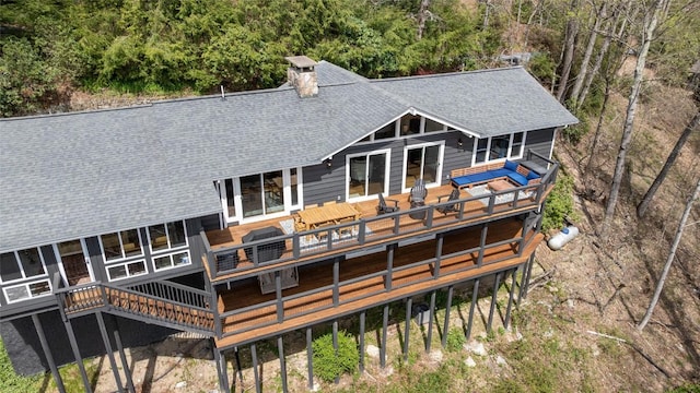 rear view of house with a wooden deck, a shingled roof, and a chimney