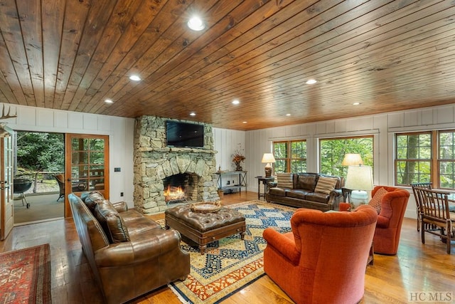 living room featuring a stone fireplace, light hardwood / wood-style flooring, and wooden ceiling