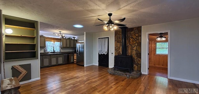 kitchen with sink, black dishwasher, a textured ceiling, a wood stove, and stainless steel fridge