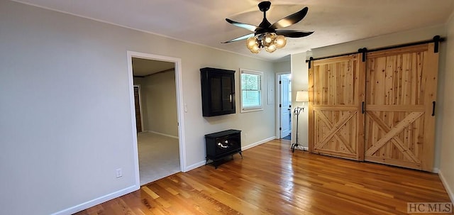 unfurnished bedroom featuring ceiling fan, wood-type flooring, a barn door, and crown molding