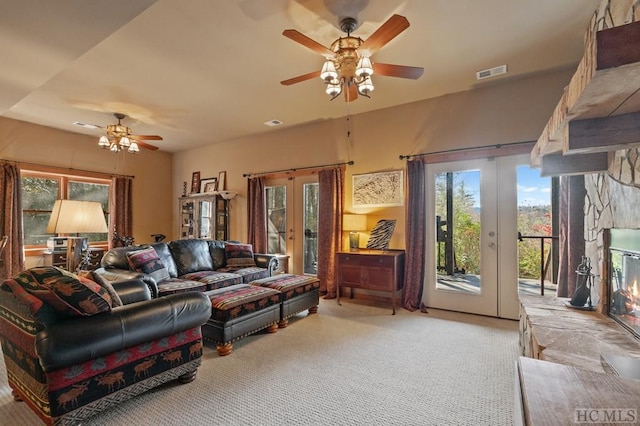 living room with french doors, ceiling fan, a stone fireplace, and carpet